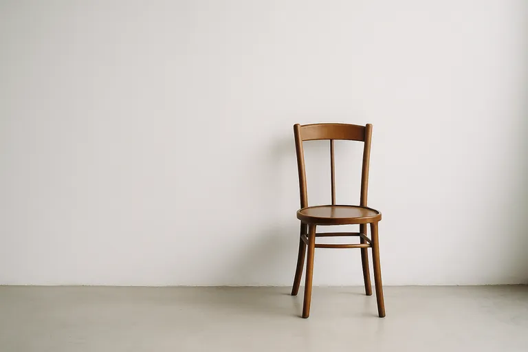 A simple wooden chair centrally placed against a large, plain white wall in a minimalist interior setting.